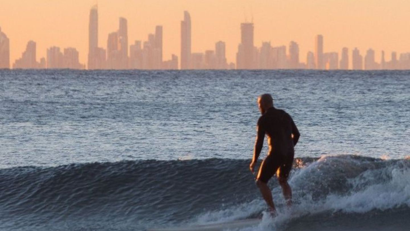 Surfer riding a wave with Surfers Paradise cityscape backdrop