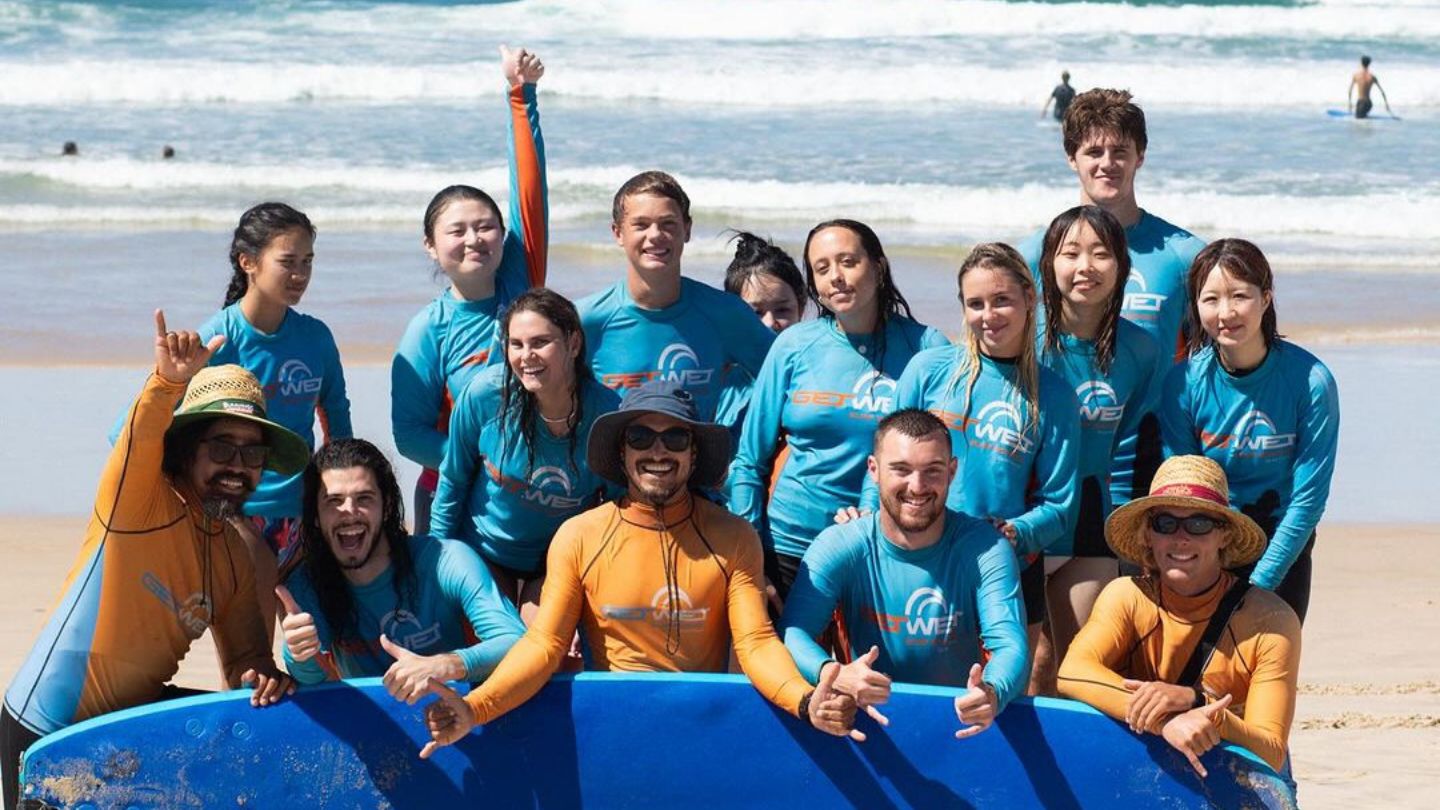 Group of hostel guests on the beach at a learn to surf class